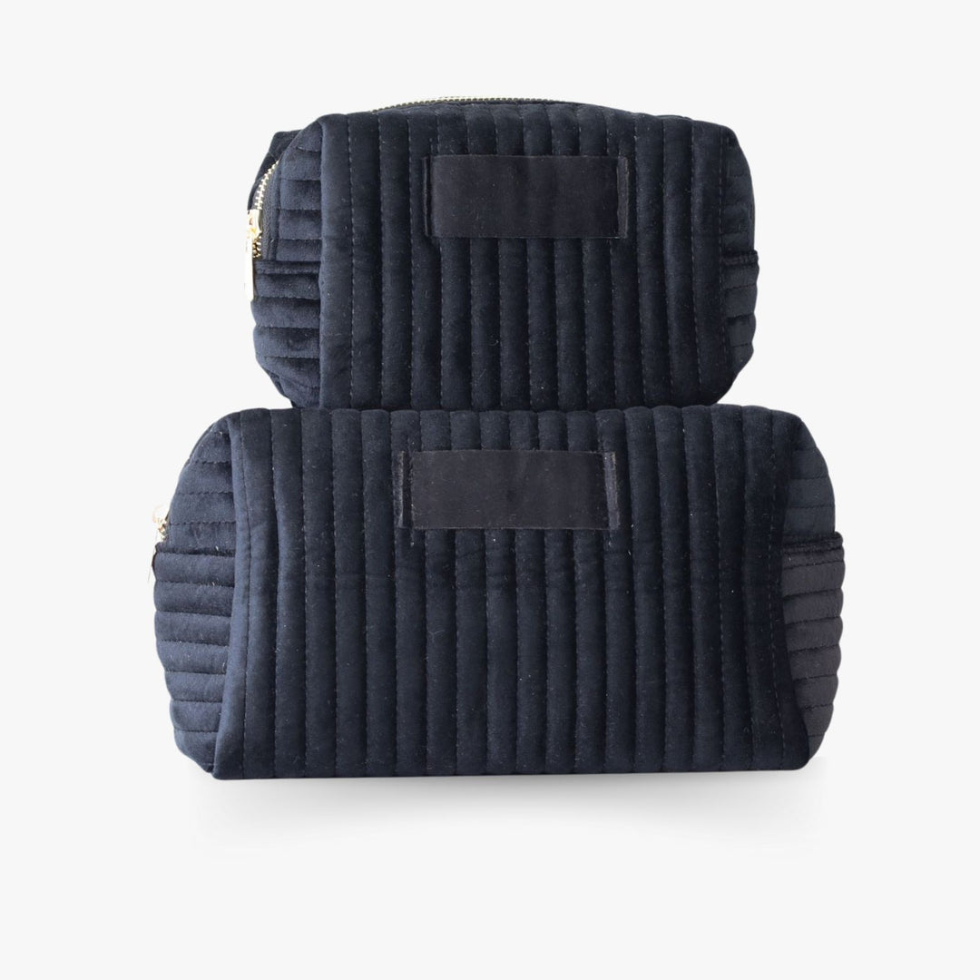 Two nesting black ribbed velvet toiletry bags with a golden zipper and a tag in the middle for monogramming.
