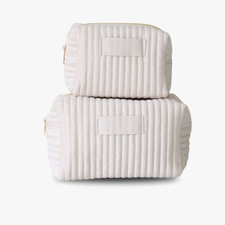 Two nesting cream ribbed velvet toiletry bags with a golden zipper and a tag in the middle for monogramming.