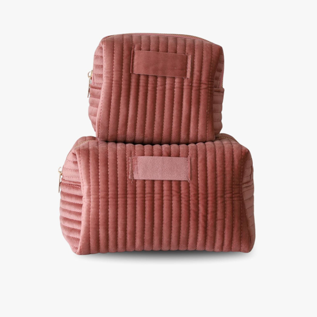 Two nesting pink ribbed velvet toiletry bags with a golden zipper and a tag in the middle for monogramming.