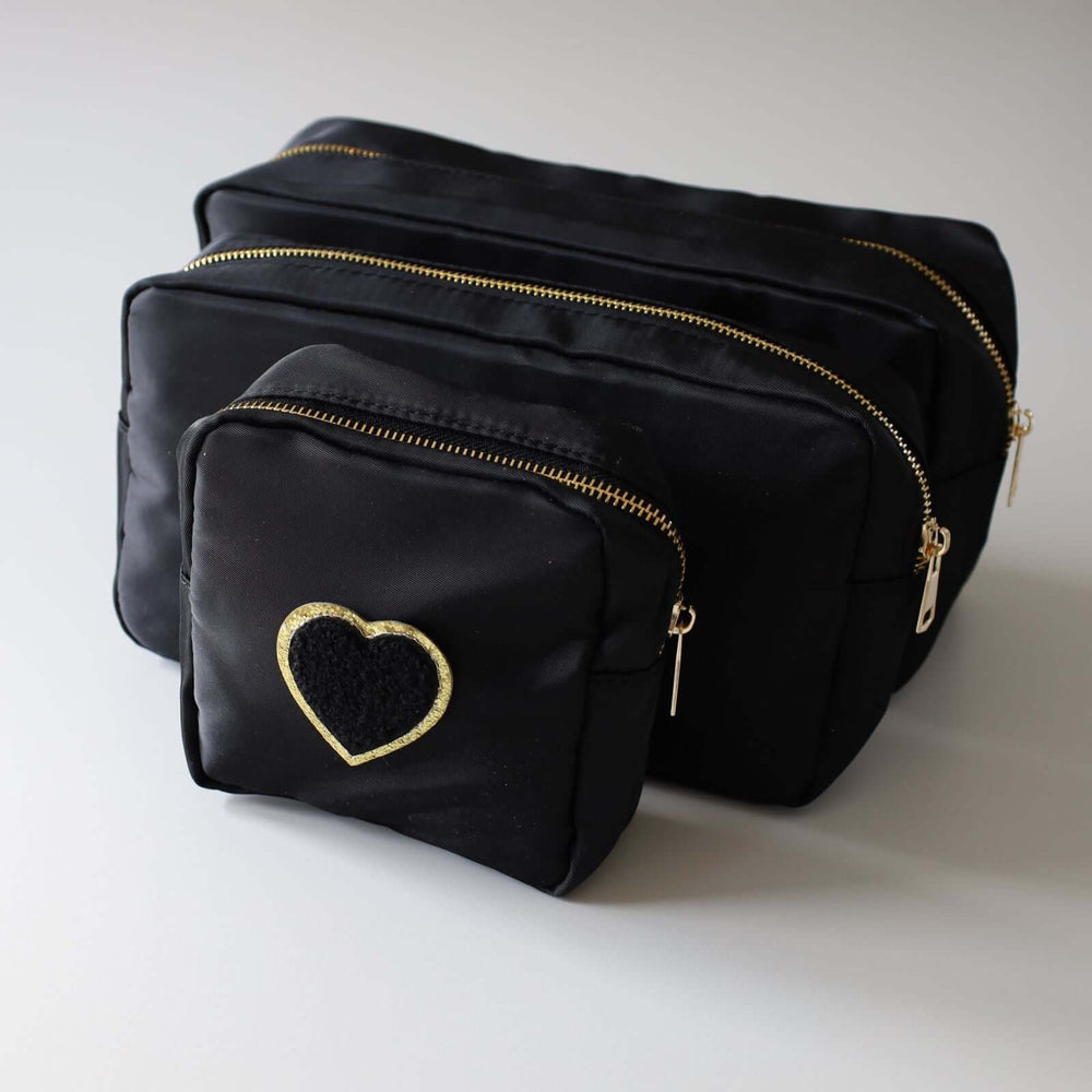 Three black nesting toiletry bags with a heart-shaped patch in the center of each. The patch is black with a gold rim. The zipper's color is gold.