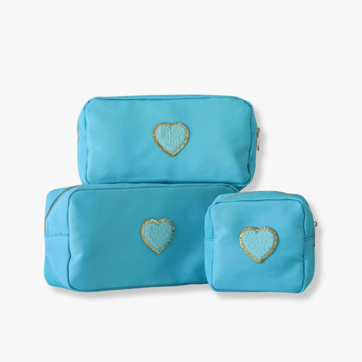 Three blue nesting toiletry bags with a heart-shaped patch in the center of each. The patch is blue with a gold rim.