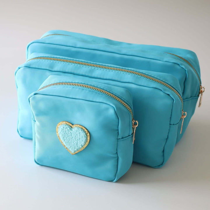 Three blue nesting toiletry bags with a heart-shaped patch in the center of each. The patch is blue with a gold rim. The zipper's color is gold.