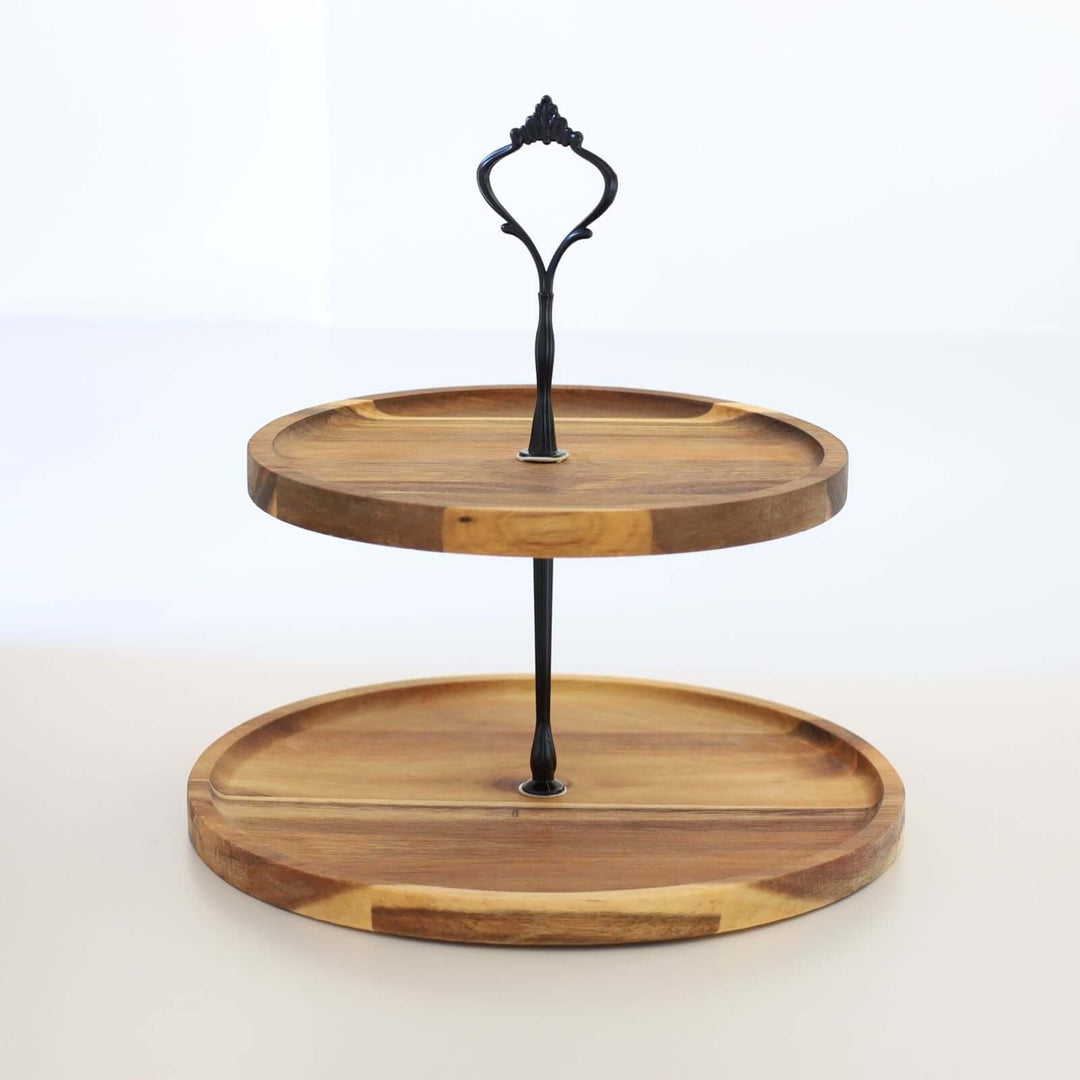 Acacia wood two-tier cake stand with a black metal handle and rod.