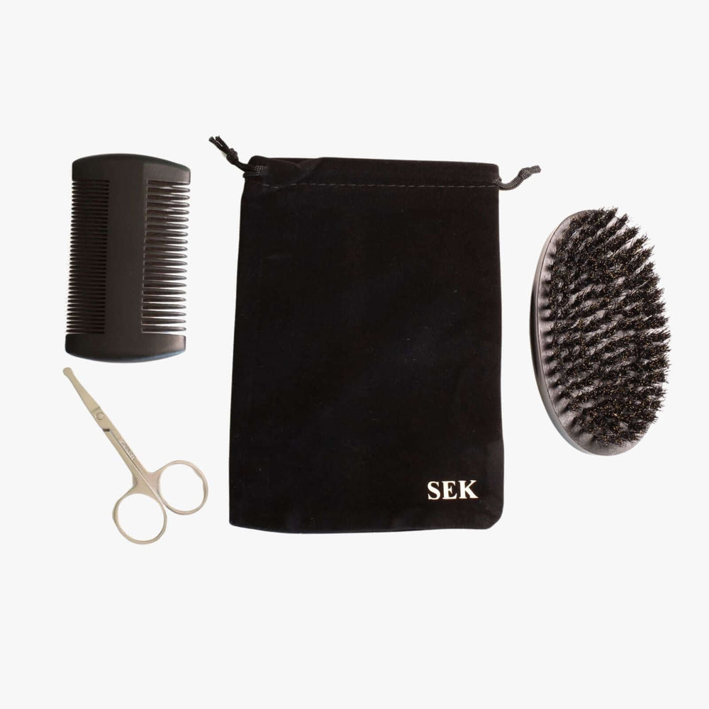 Beard grooming kit consisting of a double-sided comb, small scissors, a brush, and a monogrammed black velvet pouch.