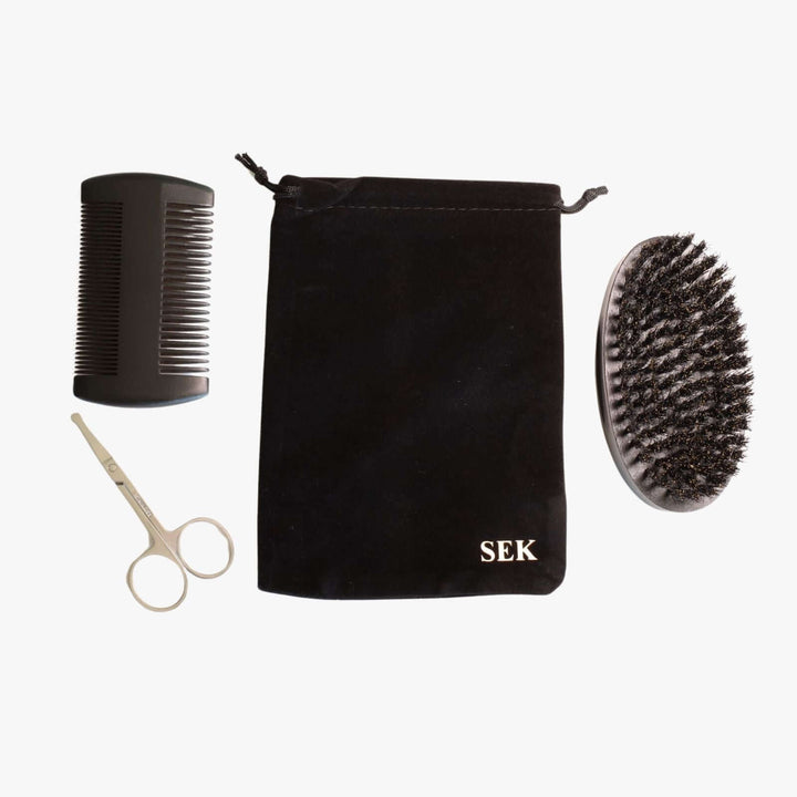 Beard grooming kit consisting of a double-sided comb, small scissors, a brush, and a monogrammed black velvet pouch.