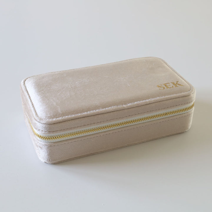 Rectangular beige velvet jewelry box with a golden zipper and initials.