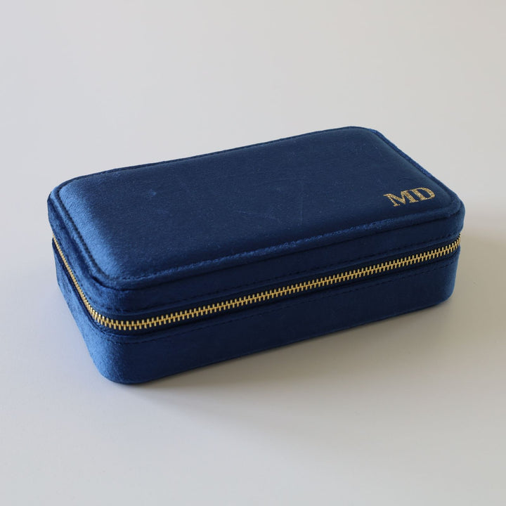 Rectangular blue velvet jewelry box with a golden zipper and initials.