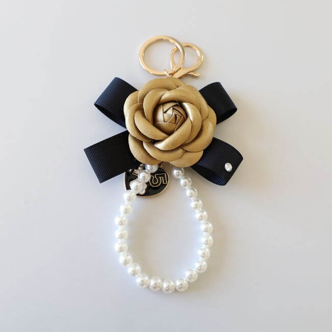 Keychain adorned with a golden camelia flower on a black ribbon and a pearl bracelet 