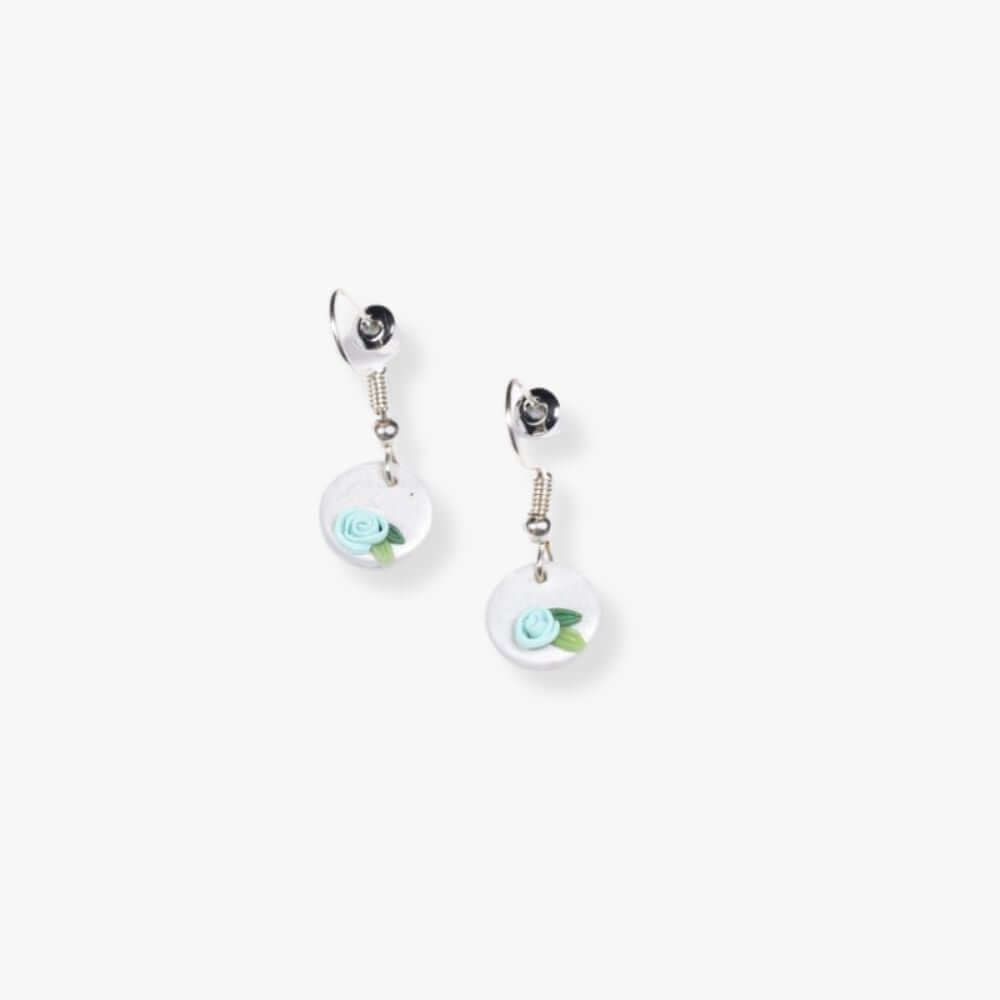 Pendant earrings with a blue flower on a round white pendant  hanging from a metal hook.