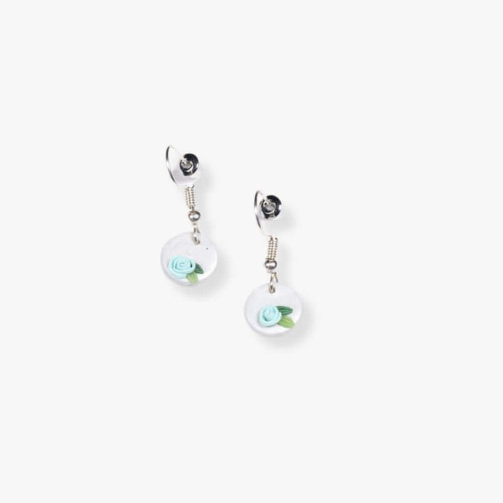 Pendant earrings with a blue flower on a round white pendant  hanging from a metal hook.