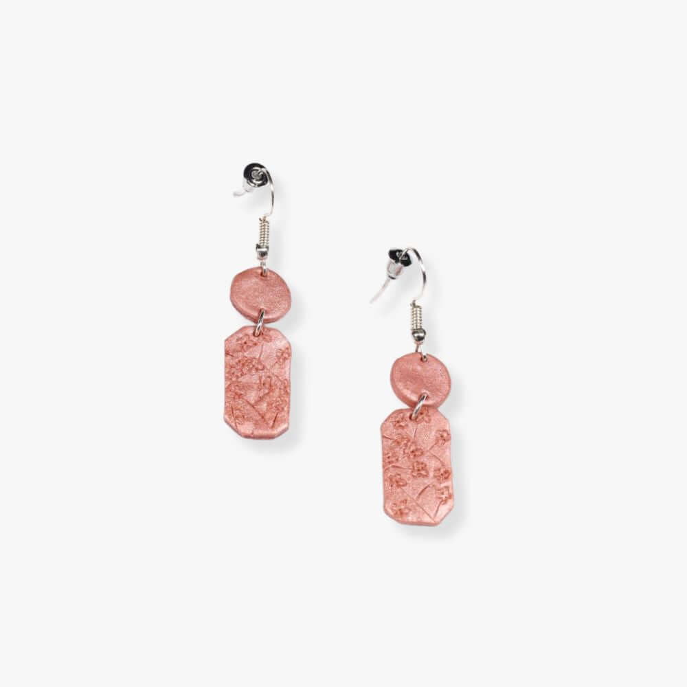 Orange earrings with a rectangular pendant connecting to a round pendant hanging from a metal hook.