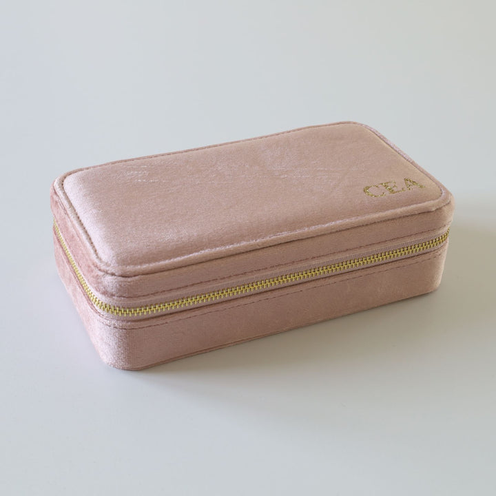 Rectangular pink velvet jewelry box with a golden zipper and initials.