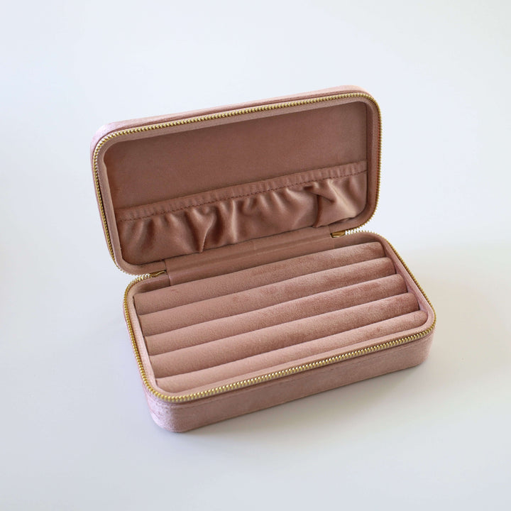 Opened pink velvet jewelry box. Inside we can see multiple slots for earrings, brooches, and rings. There is pocket attached to the lid for necklaces and bracelets.