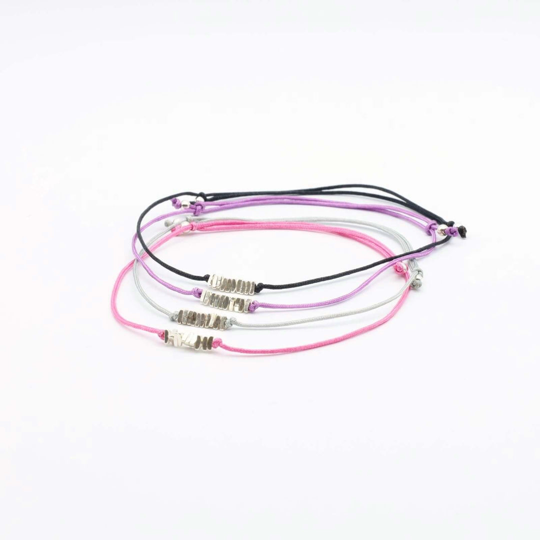 Set of 4 string bracelets in various colors: pink, black, purple and gray. Each bracelet features a string intertwined with small silver bars at the center.