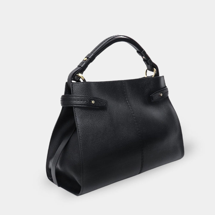 Black pebbled leather top handle bag with a leather tab on each side adorned with a gold-tone stud. Side view.