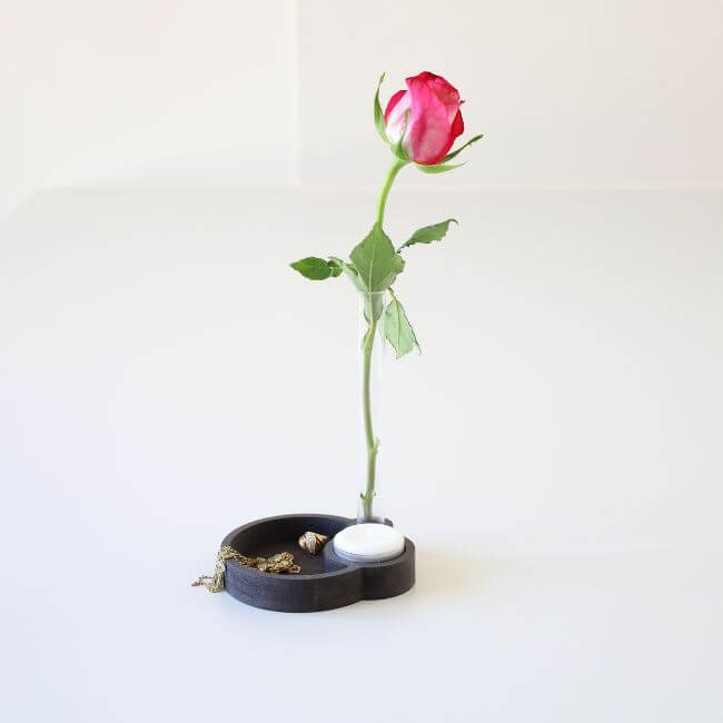 Black jewelry tray with two round compartments, one for the jewelry and one for a tealight candle. The jewelry tray holds a bud vase.