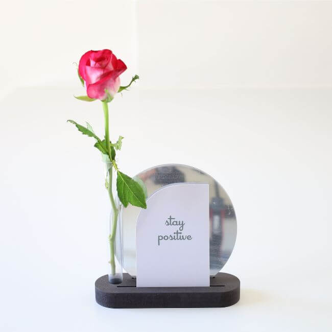 Round edge black display stand holding a bud vase, two small cards and a mirror.