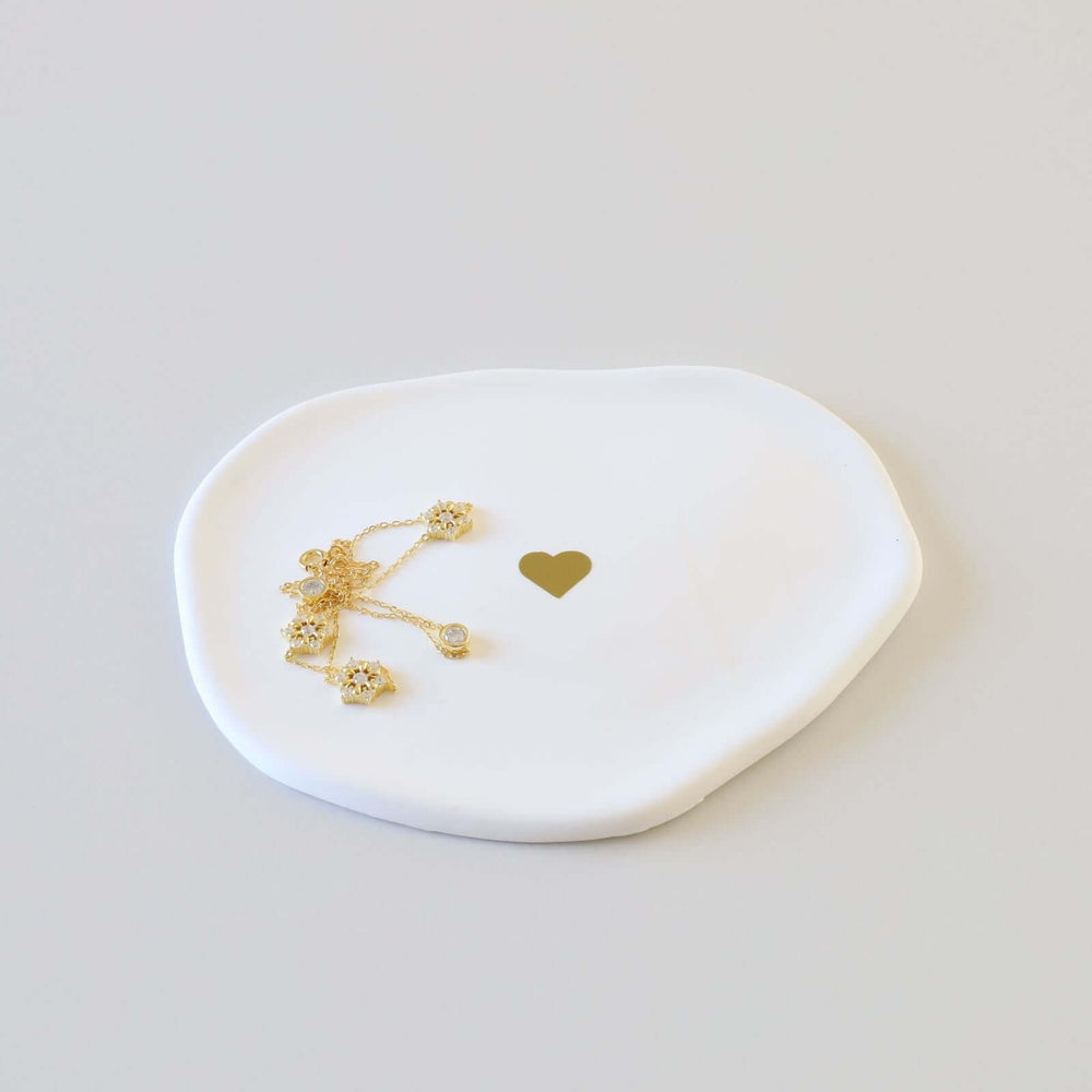 Gold bracelet on a white cloud-shaped ceramic ring dish with a golden heart at the center.