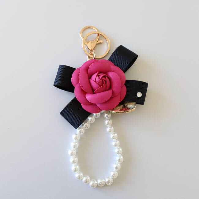 Keychain adorned with a fuscia camelia flower on a black ribbon and a pearl bracelet 