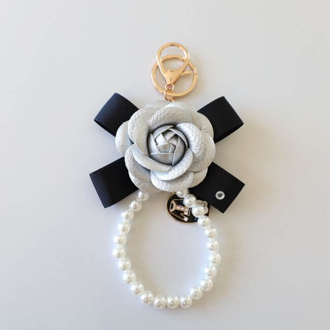 Keychain adorned with a gray camelia flower on a black ribbon and a pearl bracelet 
