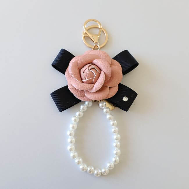 Keychain adorned with a pink camelia flower on a black ribbon and a pearl bracelet 