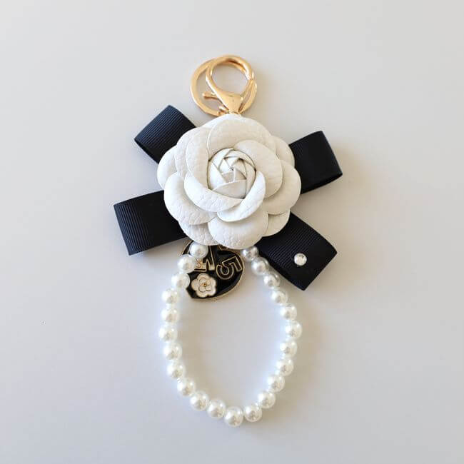 Keychain adorned with a white camelia flower on a black ribbon and a pearl bracelet 
