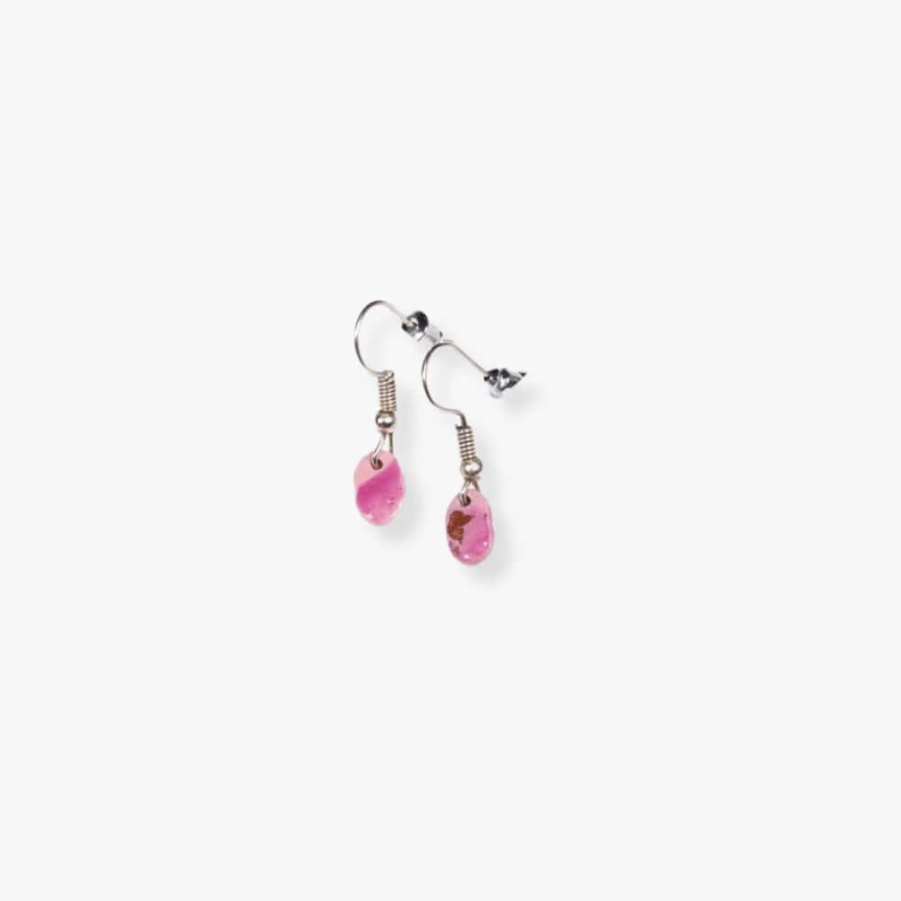 Pink drop earrings hanging from a metal hook.