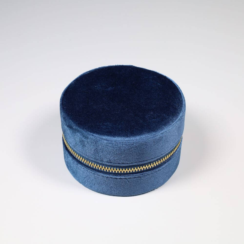 Round blue velvet jewelry box with a gold zipper.