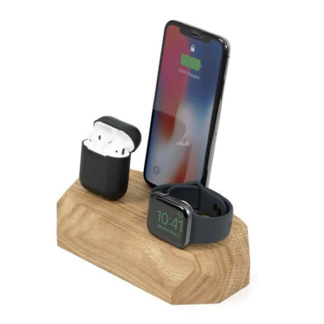 Oak charging station with an iPhone in the middle, a black Apple® Watch  on the right and Airpods in a black case on the left.