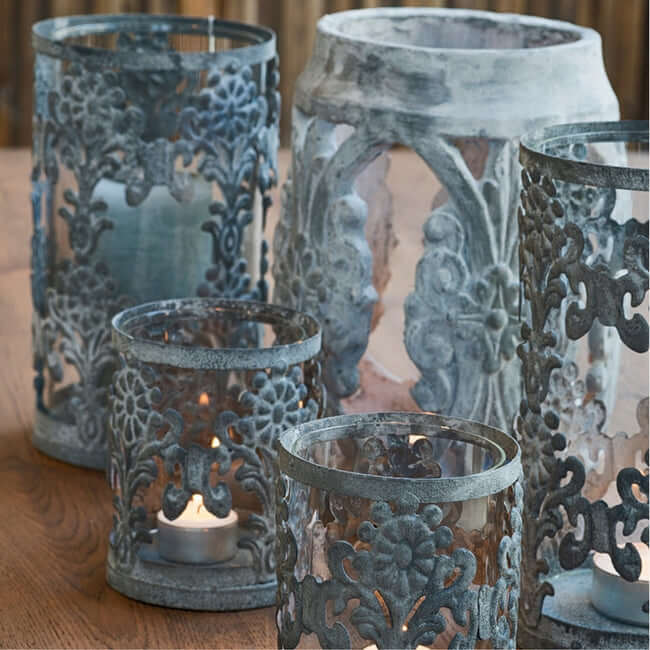 Set of two metal hurricane candle holders with glass inserts on a table.