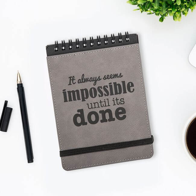 Inspirational notepad bound by a metal spiral at the top next to a black pen.