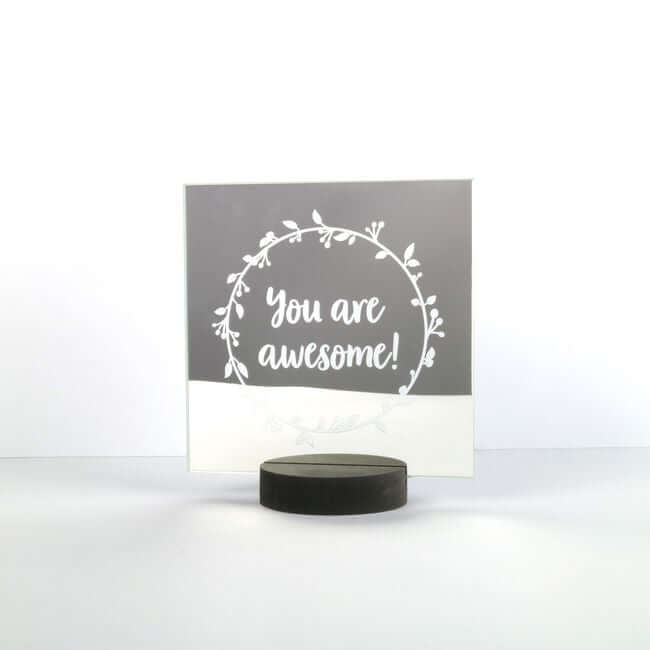 "You are awesome" message written on a square mirror placed on a round black holder.