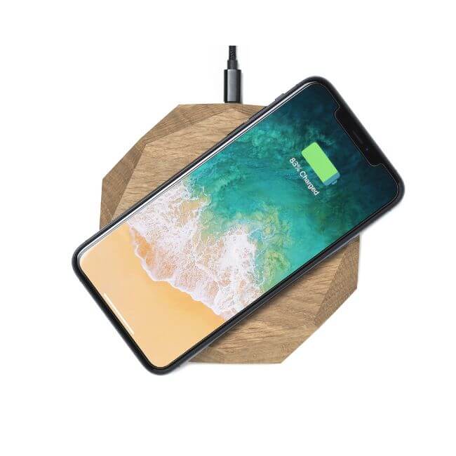Mobile phone placed on top of a wireless phone charger made from oak with a geometric design.