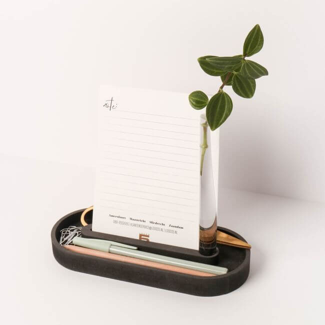 Black pen tray with round edges holding a card holder and a bud vase: side view.