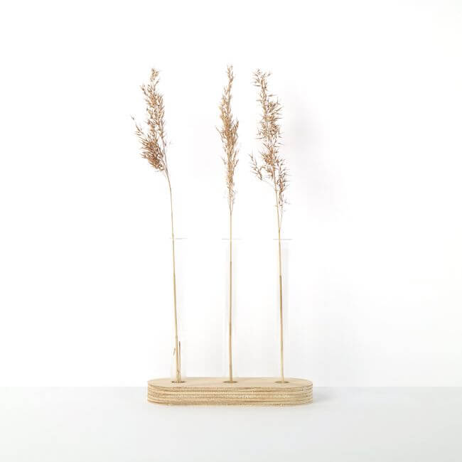 Test tube stand with 3 bud vases and dried plants on a tabletop.