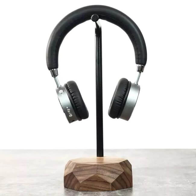 Black headphone hanging on a black metal and walnut wood headphone stand.